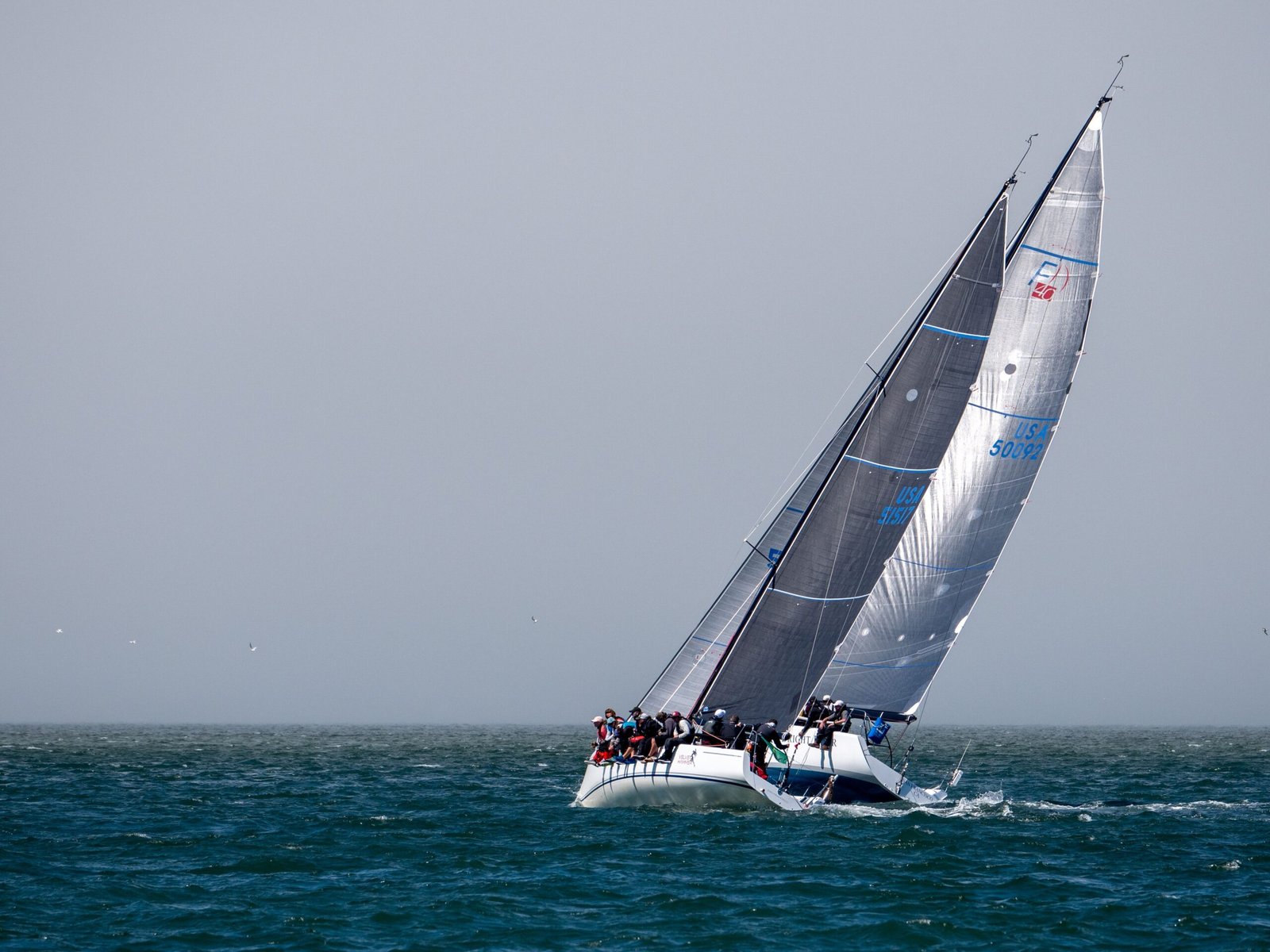 Dynamic sailing yacht with crew racing on open sea against gray sky.